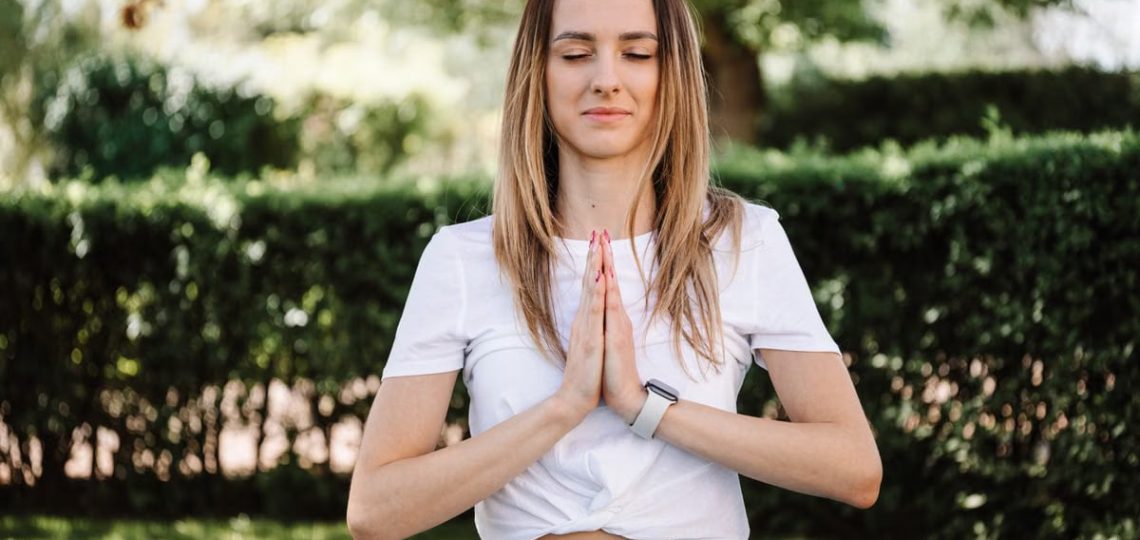 A serene moment of a woman practicing yoga with namaste pose outdoors, embracing mindfulness.